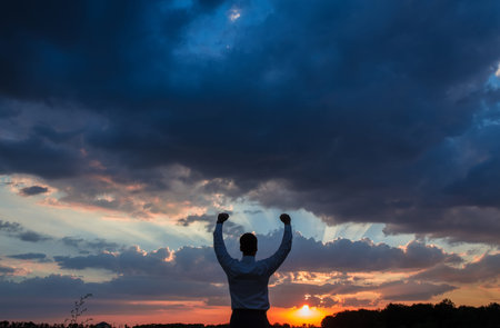 Happy businessman standing on the field to face the sunset