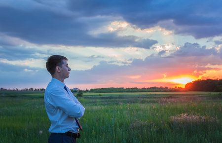 happy farmer, businessman, standing in field over wind turbines background with his hands up and thumbs upの写真素材