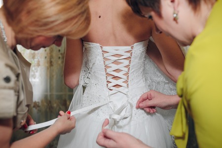 bridesmaid buttoning the dress on bride, details of beautiful lace wedding dressの写真素材