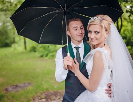 the bride and groom with a bright umbrella on a light background, the happy couple in the rain, the rain happinessの写真素材