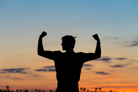 Silhouette of male celebrating with arm up towards the sunrise. Achievement concept.の写真素材