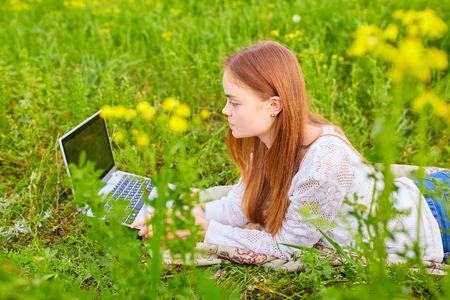 Young female lying on grass with laptop and smiling at camera.の写真素材