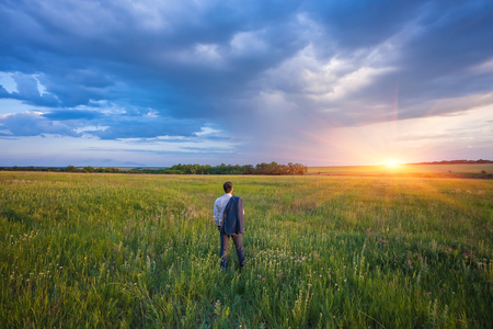 businessman in a suit with a briefcase walking on a spacious green field with a blue skyの写真素材