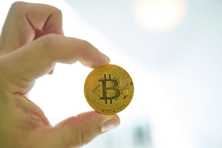 man's hand holding golden Bitcoin on Bitcoin mining background