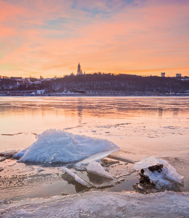 Cold Winter night cityscape with illuminated buildings in Kiev, Ukraine. The frozen Dnieper river appears in the foregroundの写真素材
