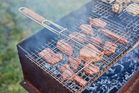 Barbecue in the forest.shashlik at nature. Process of cooking meat on barbecue, closeup. Barbecue with meat in metal grate, closed-up in forest with grassの写真素材