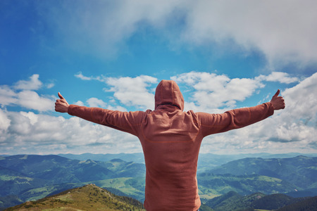 Happy tourist standing with backpack on a mountain top with raised up hands. Concept of success . Happy hiker winning reaching life goal, success, freedom and happiness, Thumbs-upの写真素材