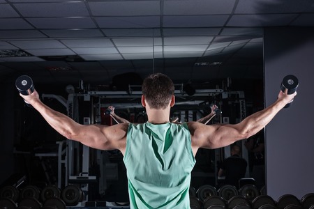 very power athletic guy bodybuilder , execute exercise with dumbbells, in dark gymの写真素材
