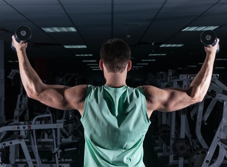 very power athletic guy bodybuilder , execute exercise with dumbbells, in dark gymの写真素材