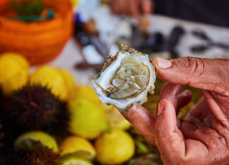 Hand in metal cut resistant glove is offering a freshly opened oyster on a fish market.