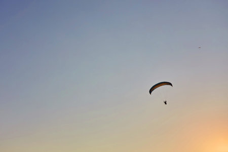 Paraglider silhouette flying over misty mountain valley in beautiful warm sunset colors - sport,...