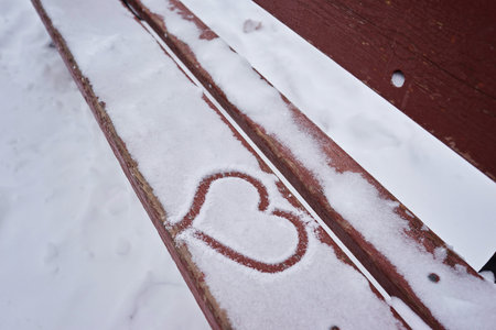 A symbol of the heart is drawn on white snow, on an orange bench. Winter holiday background