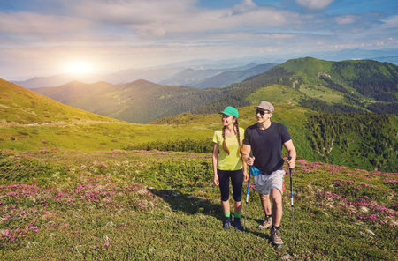 couple of hikers with backpacks enjoying panoramic view of sunset in mountains, travel and outdoor...