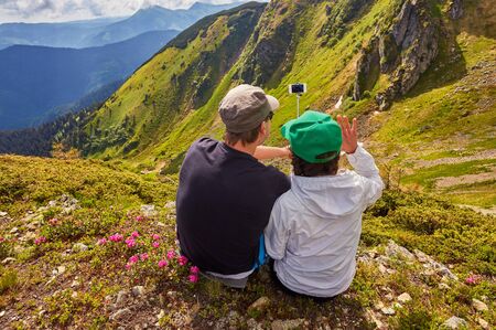 Young couple hiking taking selfie with smart phone. Happy young man and woman taking self portrait with mountain scenery in background.の写真素材