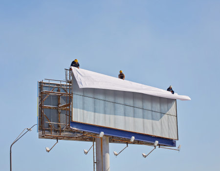 Worker prepares billboard to installing new advertisement. Industrial climber working on a ladder - placing an advertising banner.の写真素材
