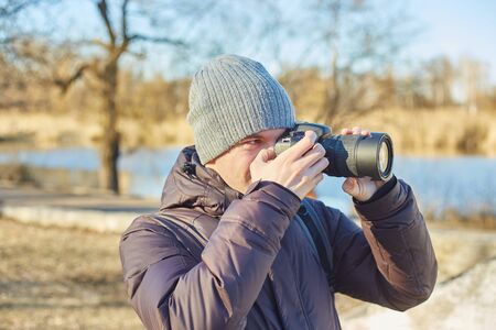 Young photographer in a hat, makes a photo on his camera in the winter parkの写真素材