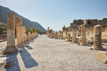 marble alley with columns leading to the Celsus Library in ancient greek city of Ephesus with mountains and clear blue sky at background with single small cloud over the Celsus Library, Turkeyの写真素材