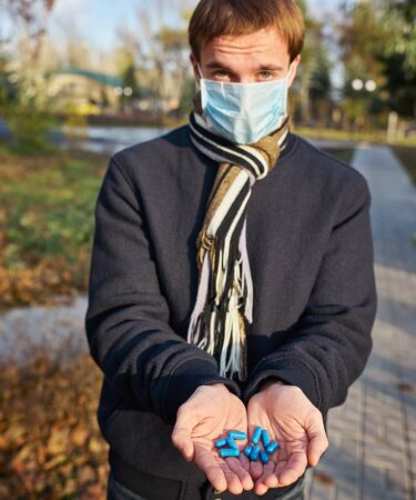 A guy in a medical mask holds out his hands with pills to the camera. Concept photo on the Covid 19 pandemicの写真素材