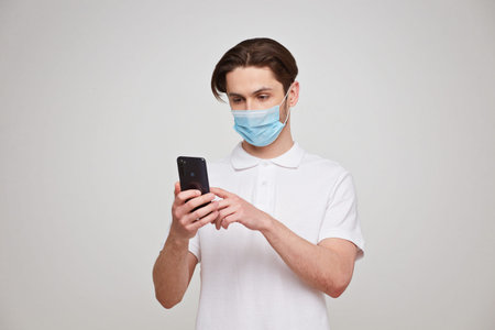 European man in a mask uses a telephone. Conceptual photo on the theme of the covid-2019 pandemic. Studio photoの写真素材