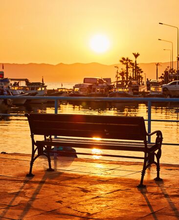 Lonely bench on the promenade near the sea at sunset timeの写真素材