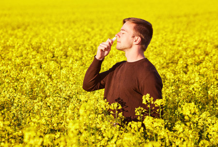 Young man in yellow canola field blowing his nose and suffering from pollen allergy.の写真素材
