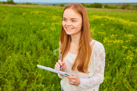 redhead girl with pen writing on notebook on grass outside