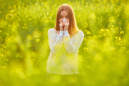 Allergic to pollen and flowering season, a redhead girl sneezing on a flower field