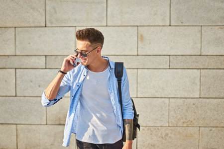 A young guy, european appearance, in sunglasses and with a black backpack. Talking on the phone on a city street.の写真素材