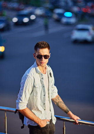 Fashionable young man in sunglasses with a black backpack walking along a city streetの写真素材