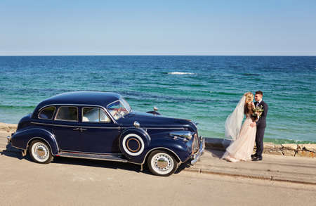 beautiful young wedding couple hugging near the car on the beach, on a sunny dayの写真素材
