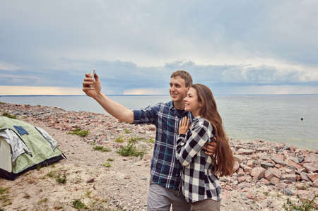 Young couple hiking taking selfie with smart phone. Happy young man and woman taking self portrait with mountain scenery in background.の写真素材