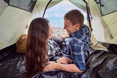 Romantic couple camping outdoors and sitting in a tent. Happy Man and woman on a romantic camping vacation.の写真素材
