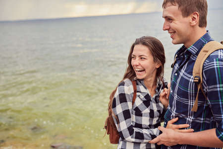 Lovers in a lake. Young couple in love sitting on the park ground near the water while these young man playing guitar in sunset time. Post processing in vintage styleの写真素材