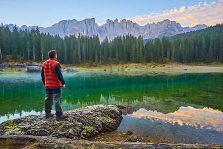 A man stands on a stone by the lake, watching the sunrise over the mountainsの写真素材