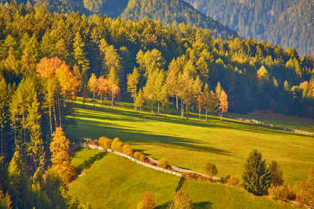 Amazing autumn scenery in Santa Maddalena village with church, colorful trees and meadows under rising sun rays. Dolomite Alps, South Tyrol, Italy.の写真素材