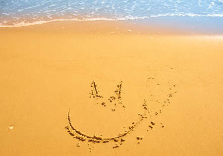 Funny smile face drawn on wet sand near seaの写真素材