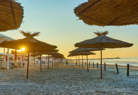 Seashore, sand beach with umbrellas and sunbeds on background of the sea and sky at dawnの写真素材