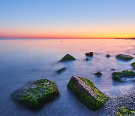 Seascape at sunset. Sea on a long shutter with stones and rocks.の写真素材