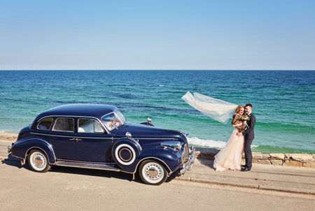 beautiful young wedding couple hugging near the car on the beach, on a sunny dayの写真素材