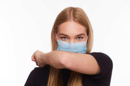 Portrait of a young woman wearing medical sterile mask, sneezing and covers with her elbow. Close up of a girl being protected from virus. Quarantine stay home conceptの写真素材
