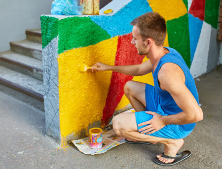 The guy paints the wall with a brush in bright colors, on the street