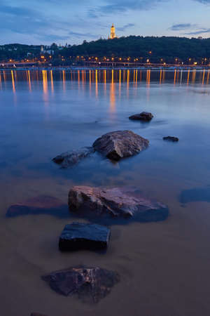 View from the right bank of the Dnieper river over the first metro bridge in Kyiv city. Evening photo, city lights are reflected in the riverの写真素材