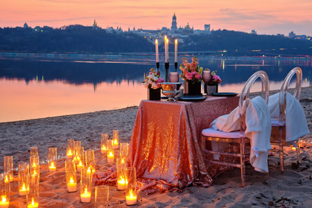 A date on the river bank, a decorated table is waiting for a couple in love. City lights in the background, evening Kyiv, Ukraine.の写真素材