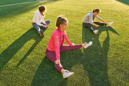 Three girls doing stretching exercises at the football stadium