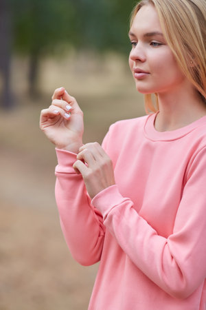 Attractive blue eyed blonde woman walk on the city park. Girl wear pink hoodie, pink bag and look happy and smiles. Portrait of a joyful young woman enjoying in autumn park. Relax in nature.の写真素材