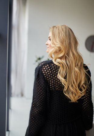 Young cute blonde posing in a studio near the window dressed in an evening black dressの写真素材