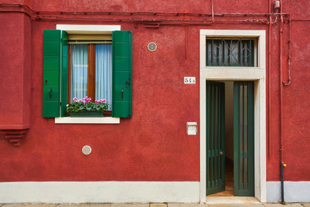 Door and window with flower on the red facade of the house. Colorful architecture in Burano island, Venice, Italy.の写真素材