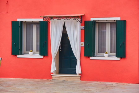 Door and window with flower on the red facade of the house. Colorful architecture in Burano island, Venice, Italy.の写真素材