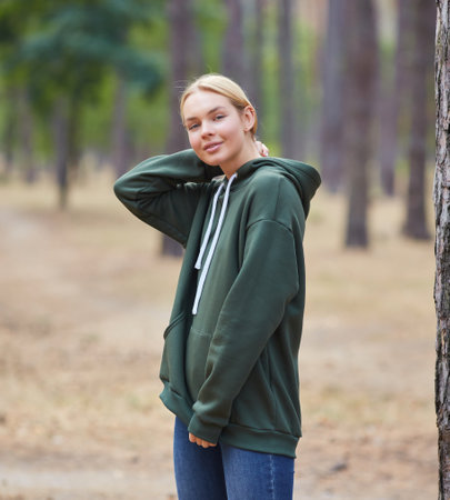 Attractive blue eyed blonde woman walk on the city park. Girl wear green hoodie, look happy and smiles. Portrait of a joyful young woman enjoying in autumn park.の写真素材