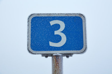 A road sign covered in frost stands on the roadside, surrounded by a misty winter landscape.の写真素材